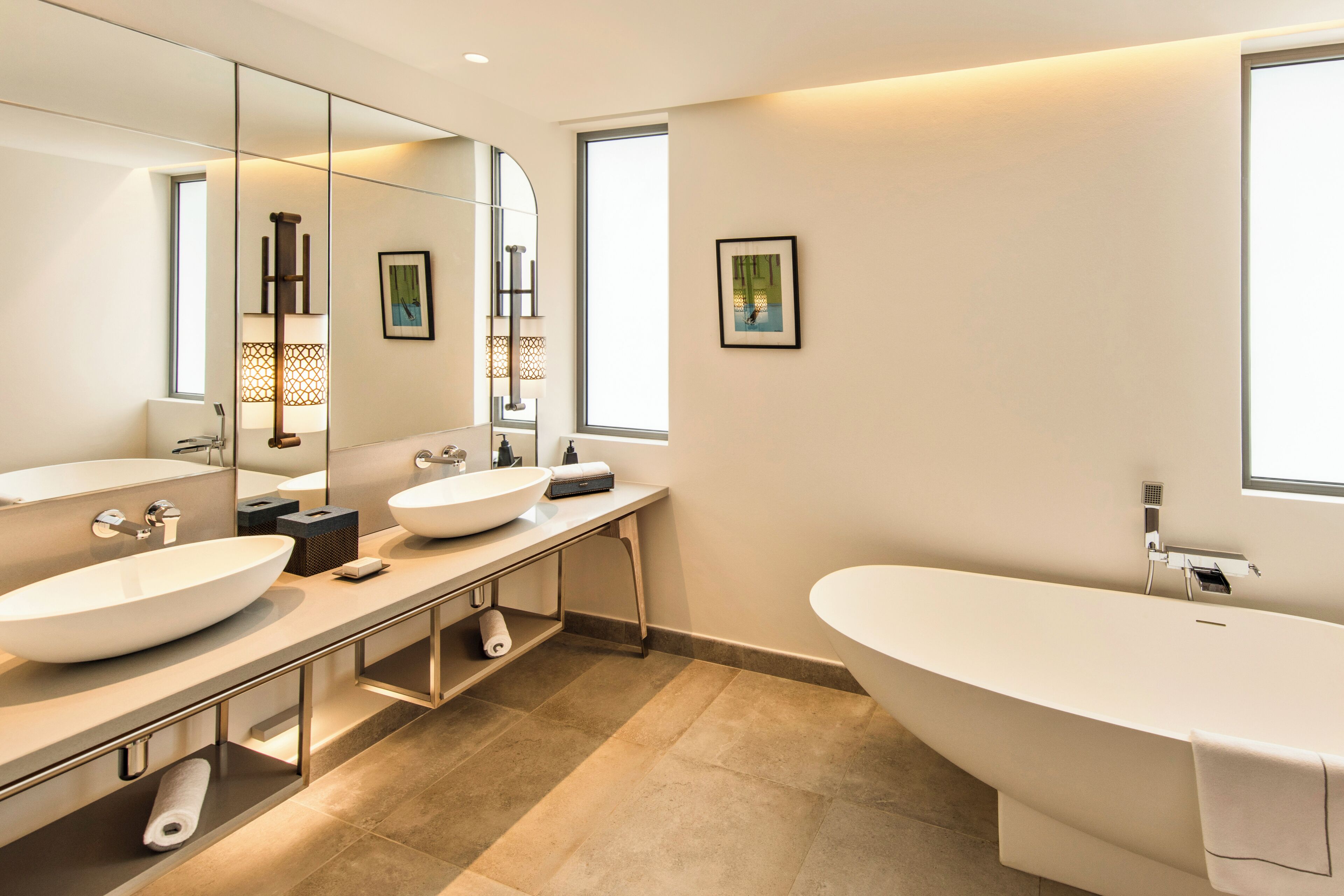 A modern bathroom with a freestanding bathtub, two sinks, a large mirror, and a window providing natural light.