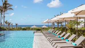 A poolside area with lounge chairs and umbrellas, a wooden deck, and a view of the ocean. - Constance Le Chaland Iko Mauritius (Blue Bay)