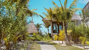 A tropical resort with a thatched-roof building, palm trees, and a stone pathway leading to a gazebo. - Constance Le Chaland Iko Mauritius (Blue Bay)