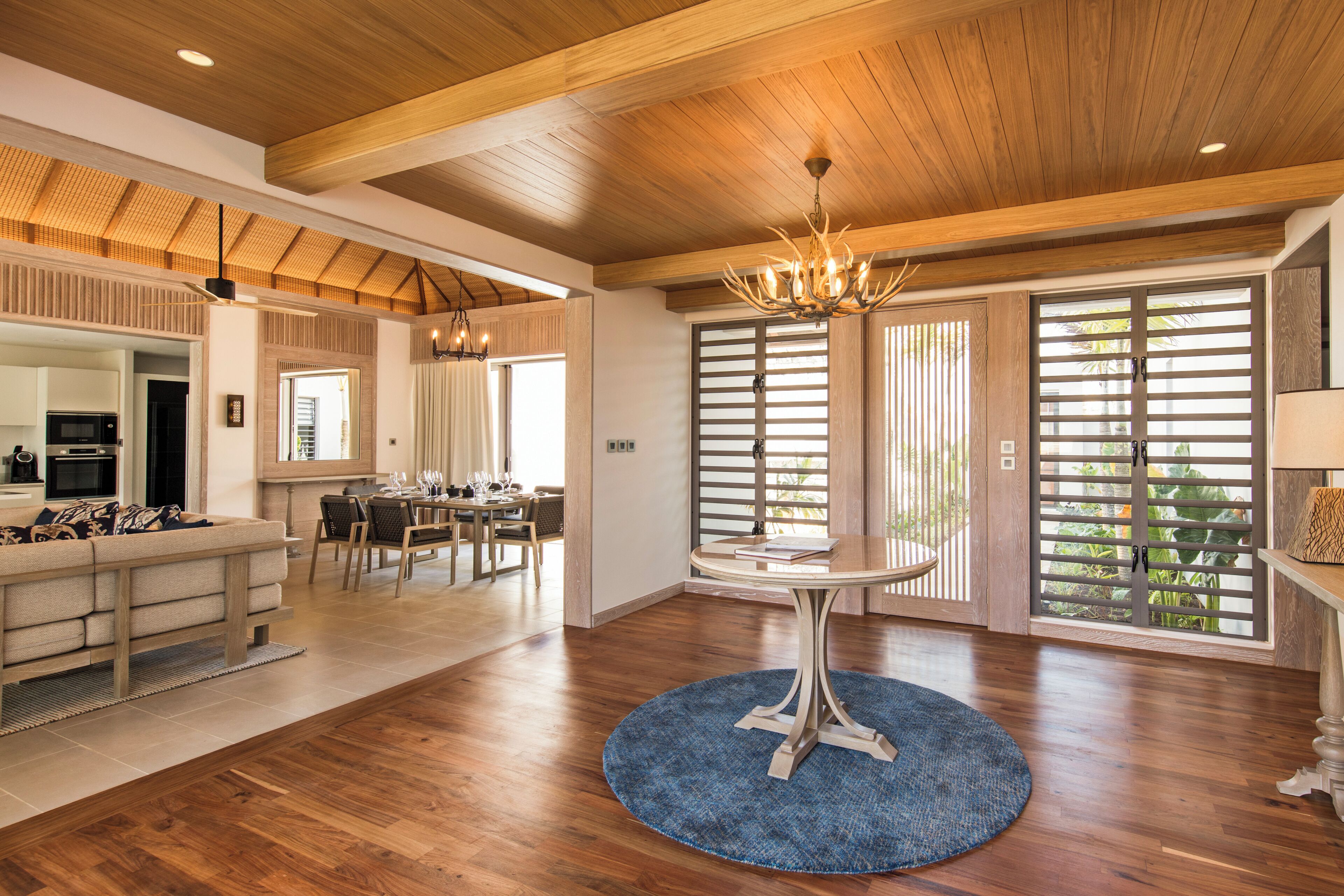 A spacious living area with a wooden ceiling, a dining table, and a large window with a view of greenery.
