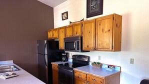 A compact kitchen with wooden cabinets, a refrigerator, a microwave, an oven, and a sink.