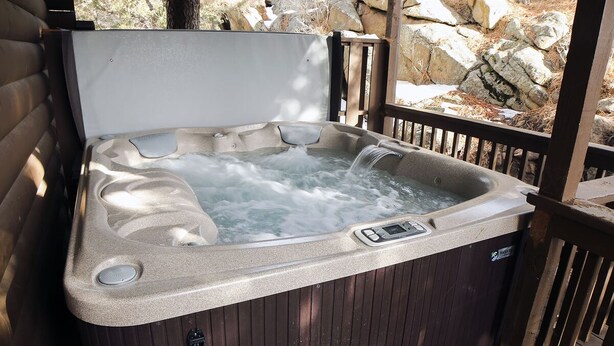 A hot tub with a wooden deck and a rocky landscape in the background.