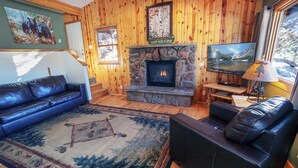A cozy living room with a stone fireplace, wooden walls, a blue leather sofa, and a television.