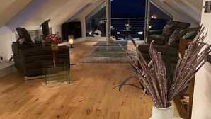 An attic room with a high ceiling, wooden flooring, a glass table, and a seating area with a sofa and chairs. - Invercreran Lodge Luxury Bed & Breakfast (Appin)