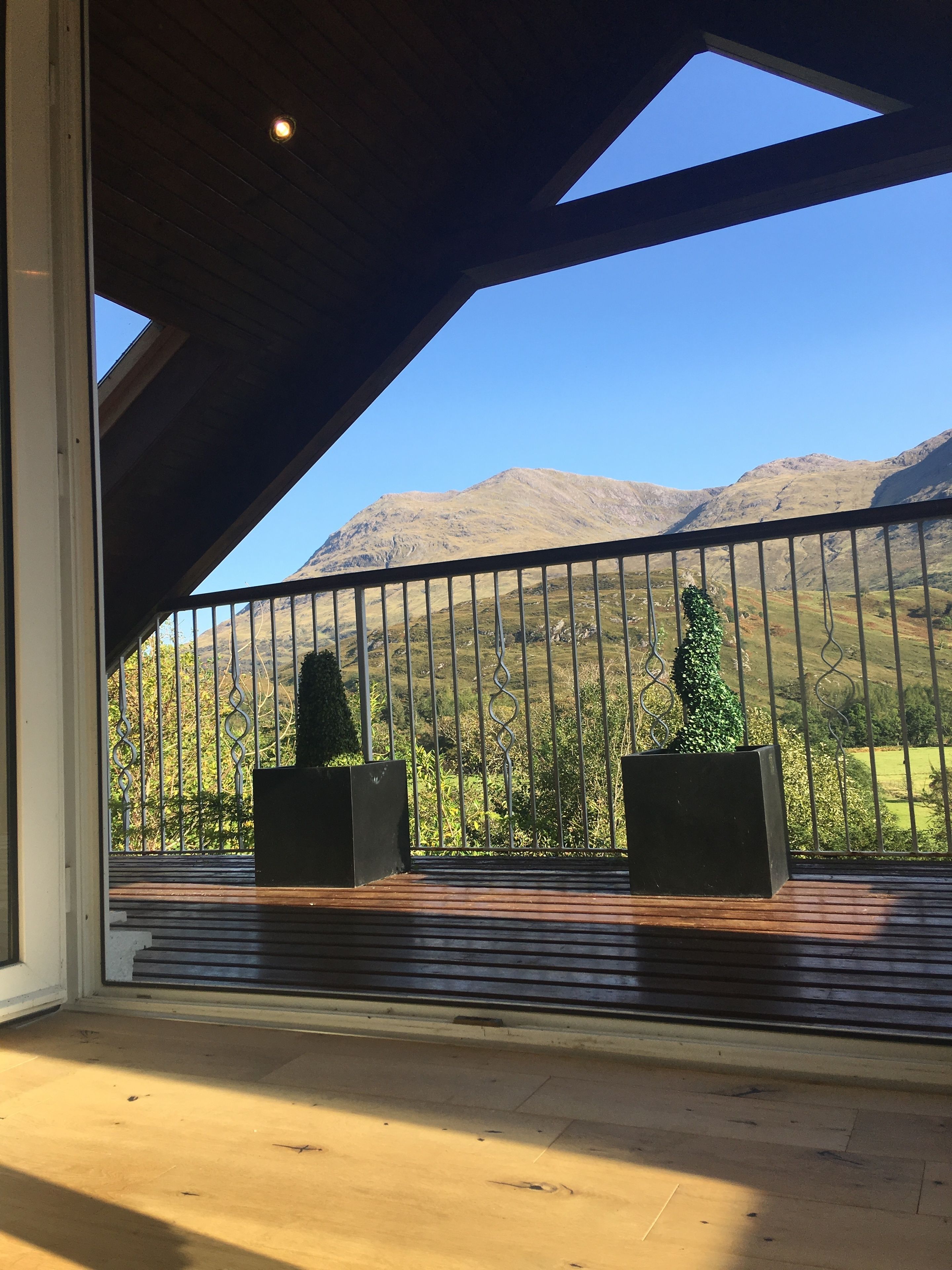 A balcony with a view of mountains, wooden flooring, and metal railings.