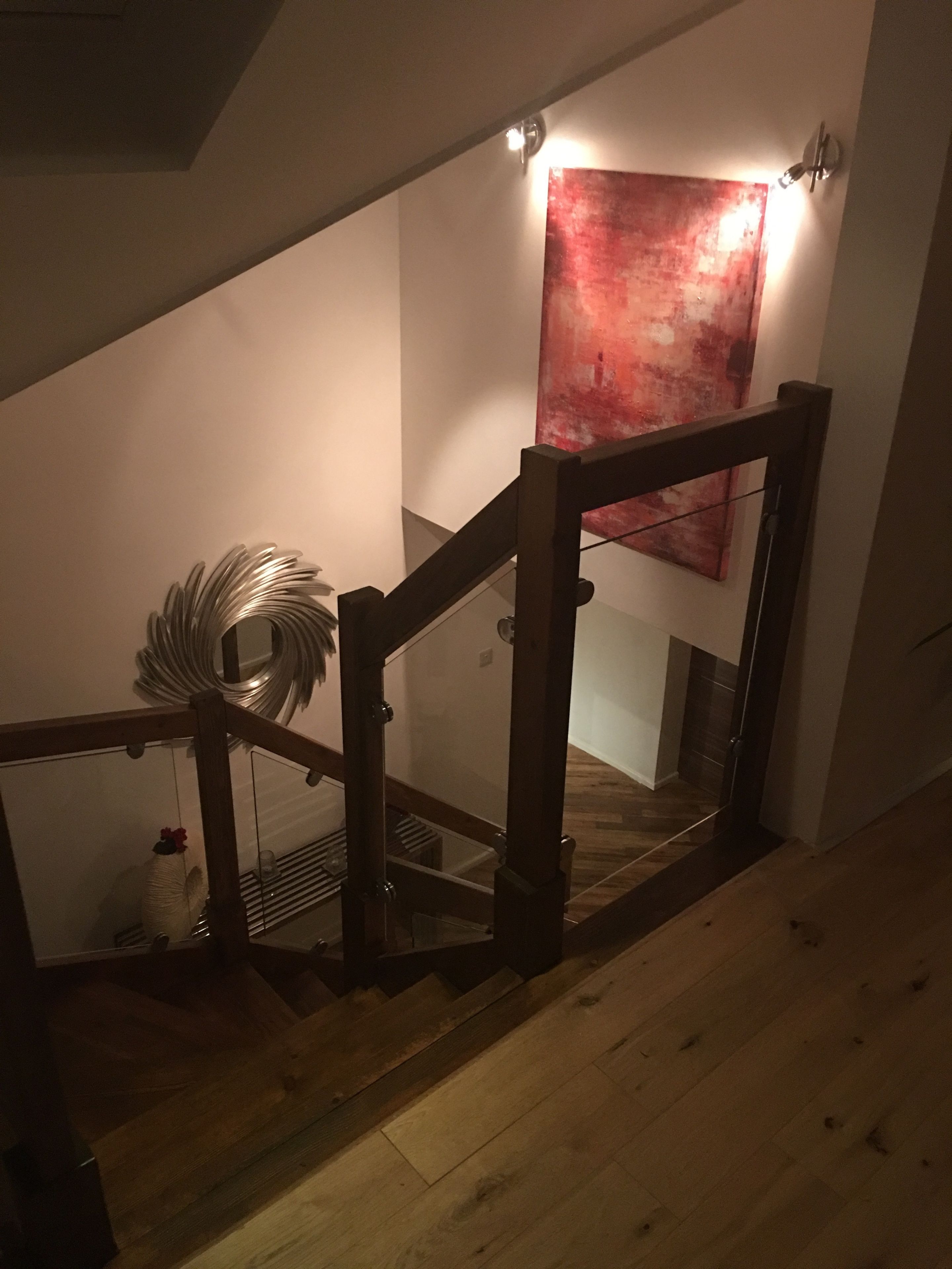 En trætrap med gelænder af glas, et rødt abstrakt maleri på væggen og en dekorativ metalkulptur på gulvet.