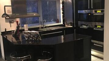 A modern kitchen with a central island, stainless steel appliances, and a window with blinds.