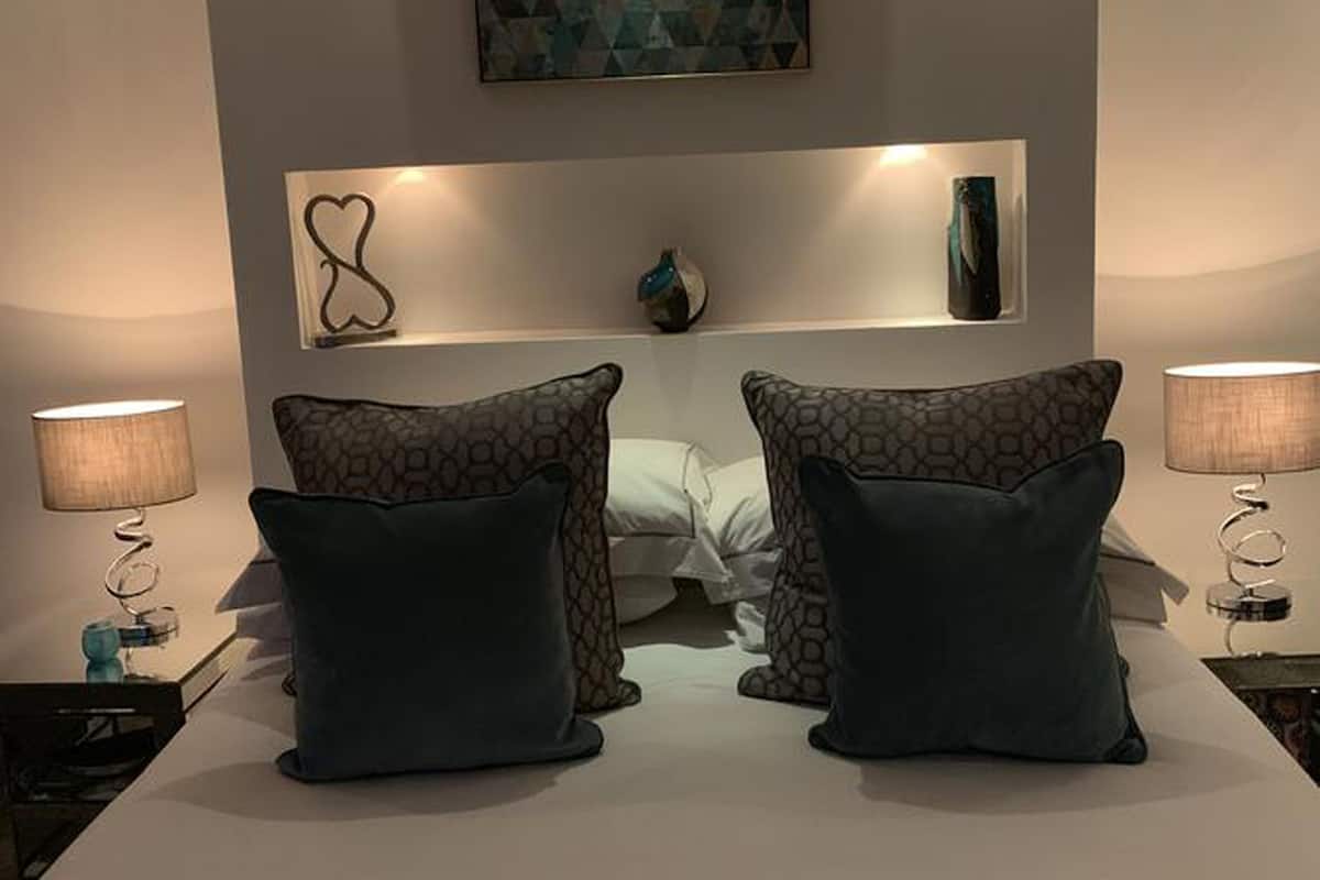 A hotel room with a large bed, two bedside lamps, a geometric wall art piece, and a small decorative item on the nightstand.