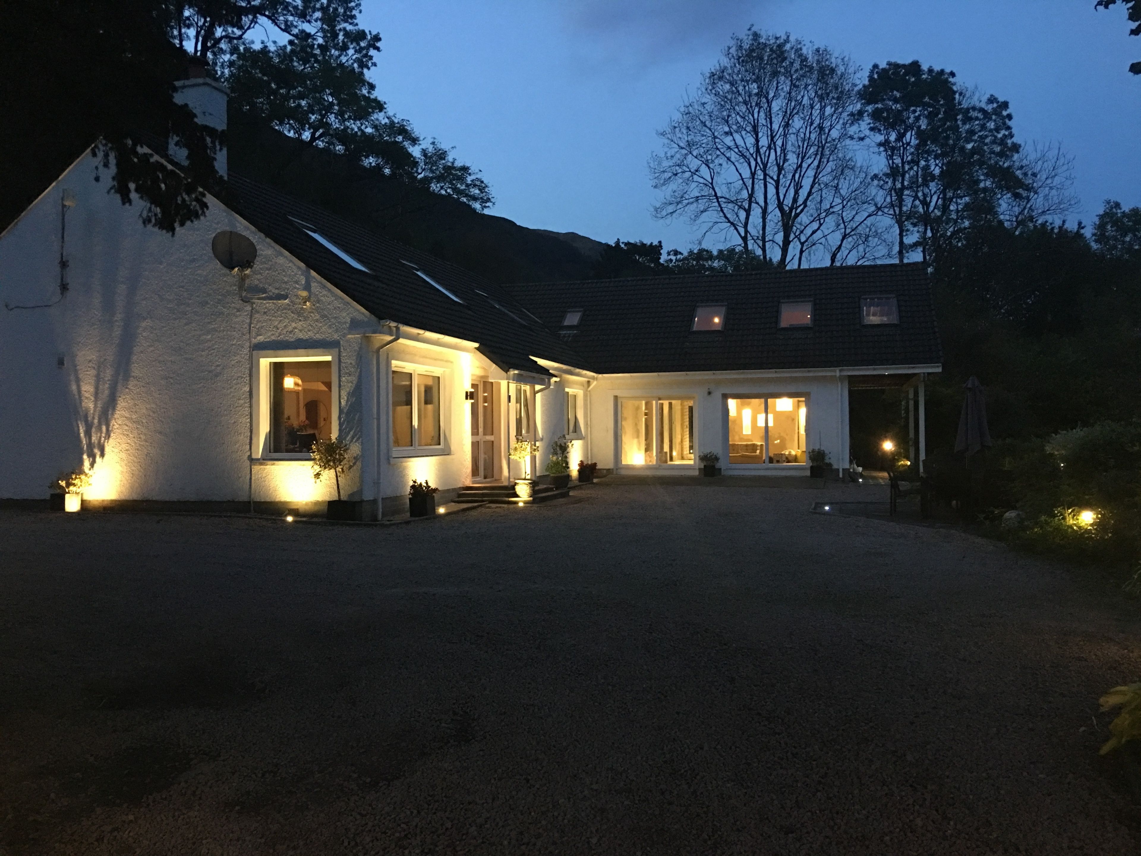 A two-story house with a gravel driveway and a well-lit front porch.