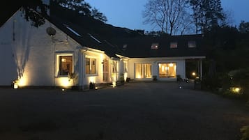 A two-story house with a gravel driveway and a well-lit front porch.