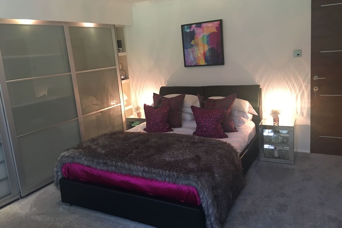 A bedroom with a bed, a wardrobe, a nightstand, and a painting on the wall.