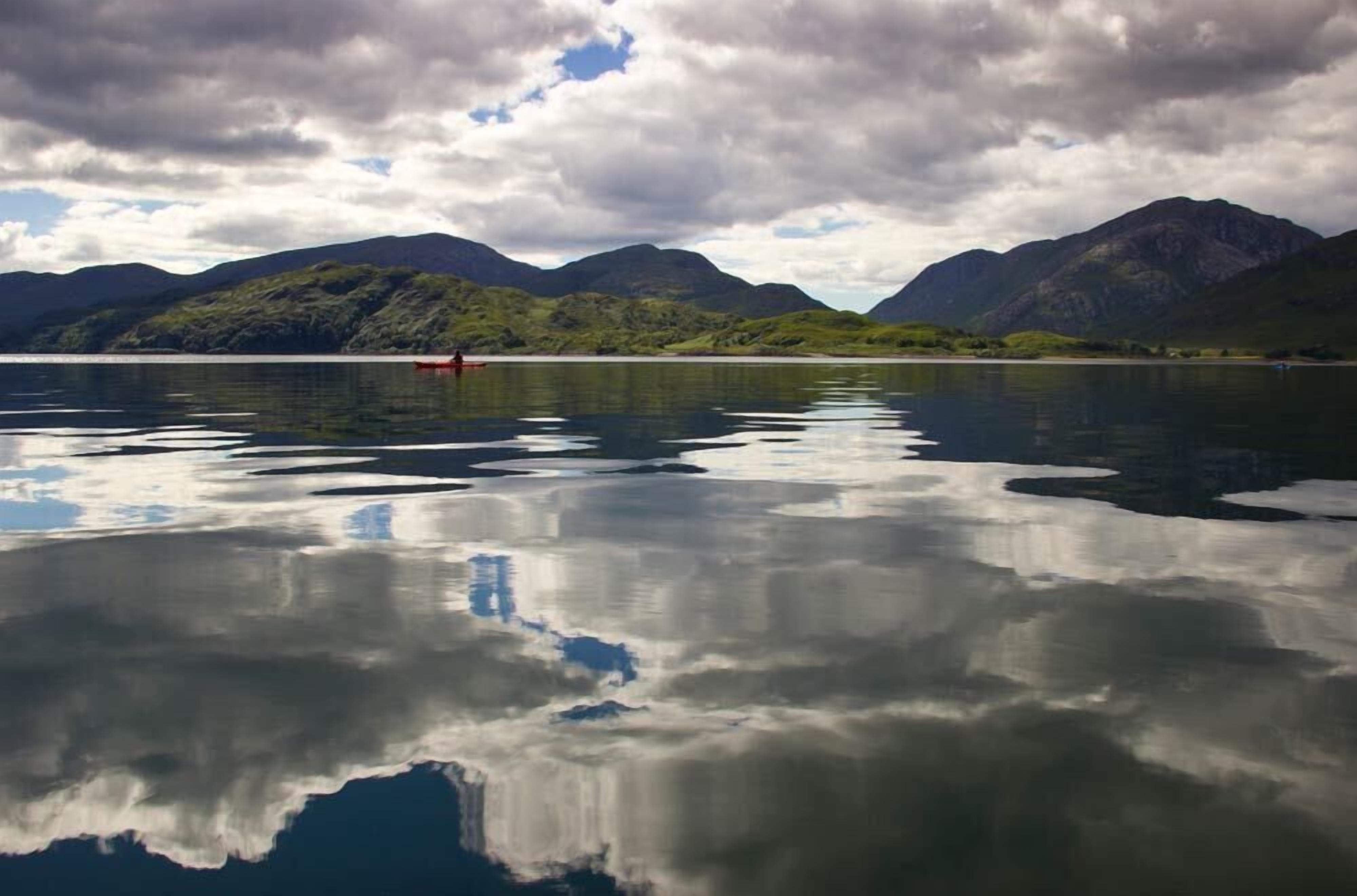 Un lago tranquilo con montañas al fondo y un barco rojo en el agua.