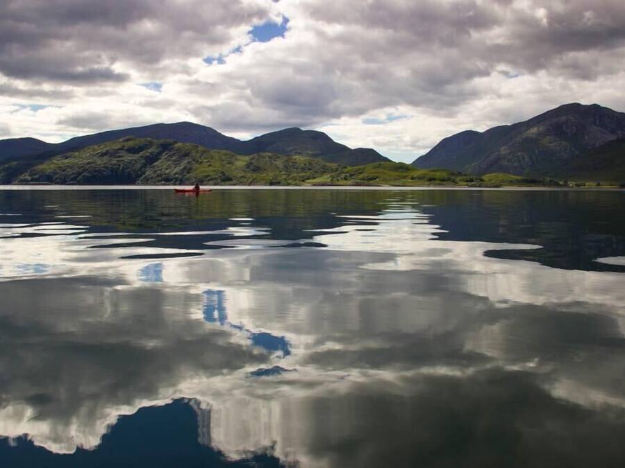 Un lago tranquilo con montañas al fondo y un barco rojo en el agua.