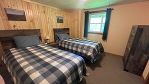 A room with two beds, wooden walls, a window with curtains, and a ceiling light. - Riverside Cottage near snowmobile and atv trails and Mt. Bohemia with Wi-Fi! (Eagle River)