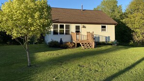 A single-story house with a front porch, a small deck, and a well-maintained lawn. - Riverside Cottage near snowmobile and atv trails and Mt. Bohemia with Wi-Fi! (Eagle River)