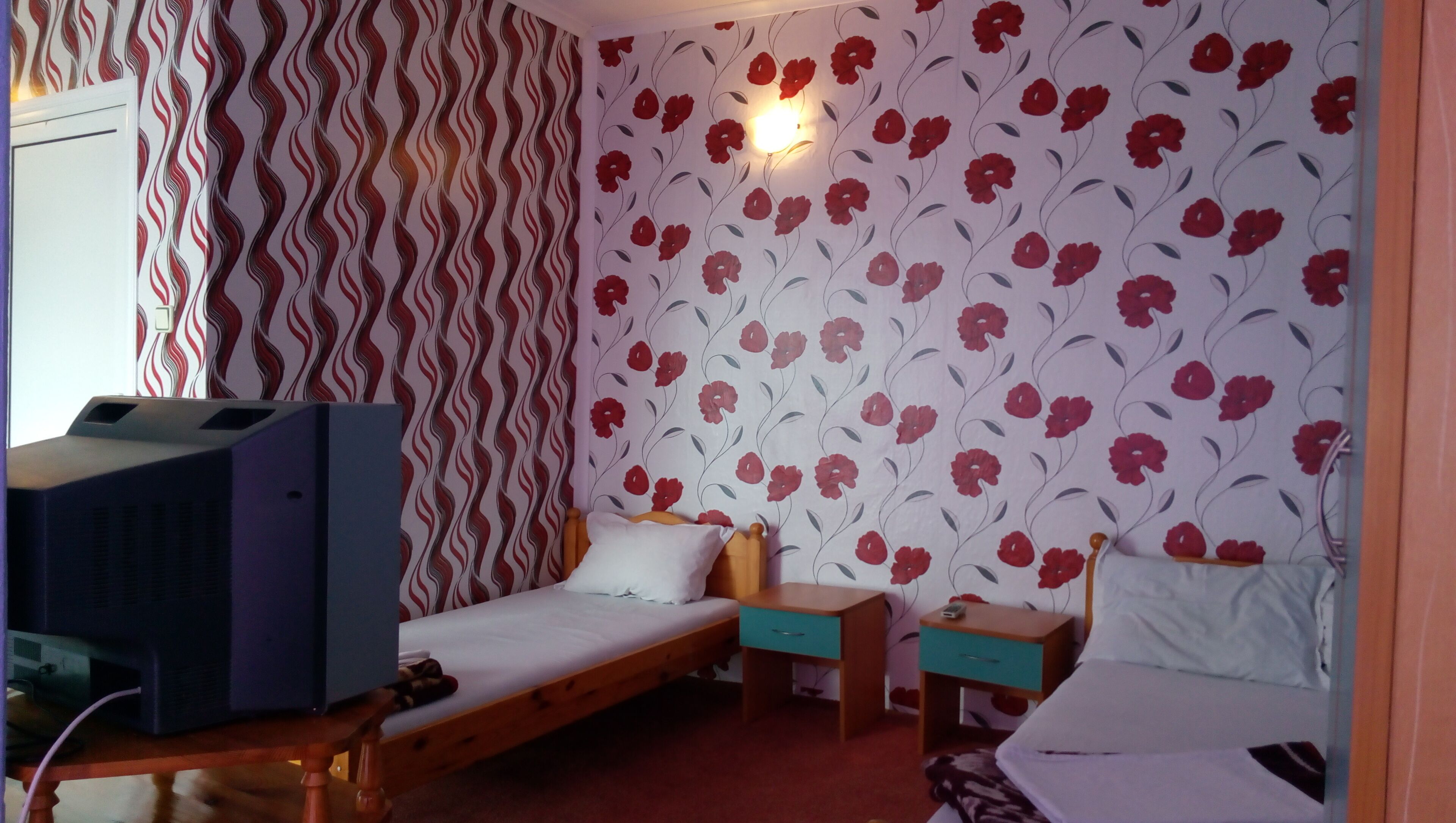 A bedroom with two single beds, a wooden desk, a nightstand, and a television.