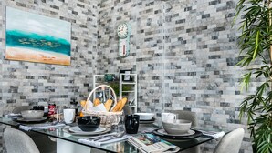 A modern dining area with a glass table, grey chairs, and a tiled wall with a clock and artwork. - Diaphanous Urban Apartment (Panama City)