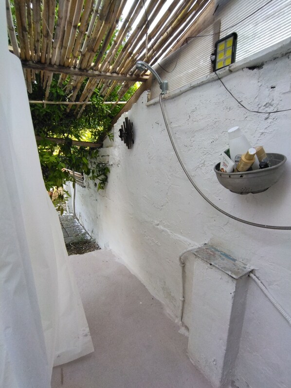 A narrow corridor with a bamboo ceiling, a white wall, and a small shelf with toiletries.
