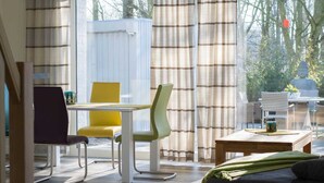 A modern living room with a sofa, a dining table with chairs, and a view of a garden. - Holiday home beach runner - beach runner (Niebüll)