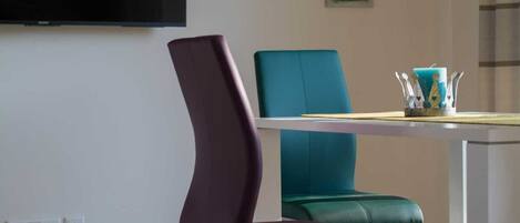 A modern dining area with a white table and two chairs, one purple and one teal.