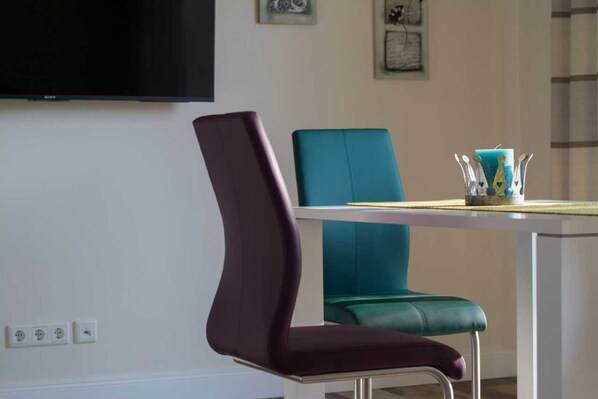 A modern dining area with a white table and two chairs, one purple and one teal. - Holiday home beach runner - beach runner (Niebüll)