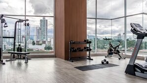 A spacious gym with a city view, featuring a bench, dumbbells, an exercise bike, and a treadmill. - Enchanting Ocean View (Panama City)