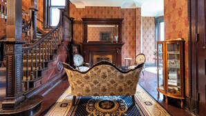 Un'imponente scalinata con ringhiere elaborate, un grande specchio sopra un camino e una vasca da bagno d'epoca in una stanza riccamente decorata.