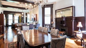 Un'ampia sala da pranzo con un grande tavolo in legno e sedie decorate, un lampadario e un camino.