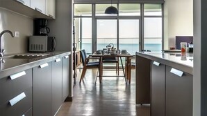 Une cuisine moderne avec vue sur la mer, équipée d’une machine à café, d’une table à manger avec des chaises et d’une grande fenêtre.