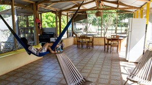 A covered patio with a hammock, a grill, and a dining area with chairs and a table. - Backpackers Paradise (Sarteneja)