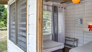 A room with two beds, a window with a curtain, a small table, and a red lamp. - Backpackers Paradise (Sarteneja)