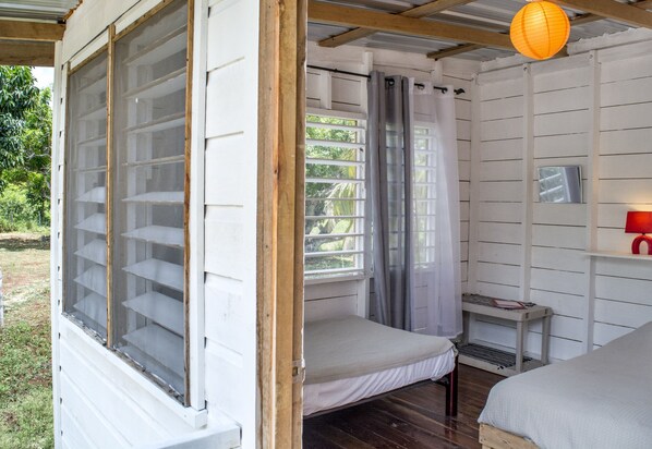 Une chambre avec deux lits, une fenêtre avec un rideau, une petite table et une lampe rouge.