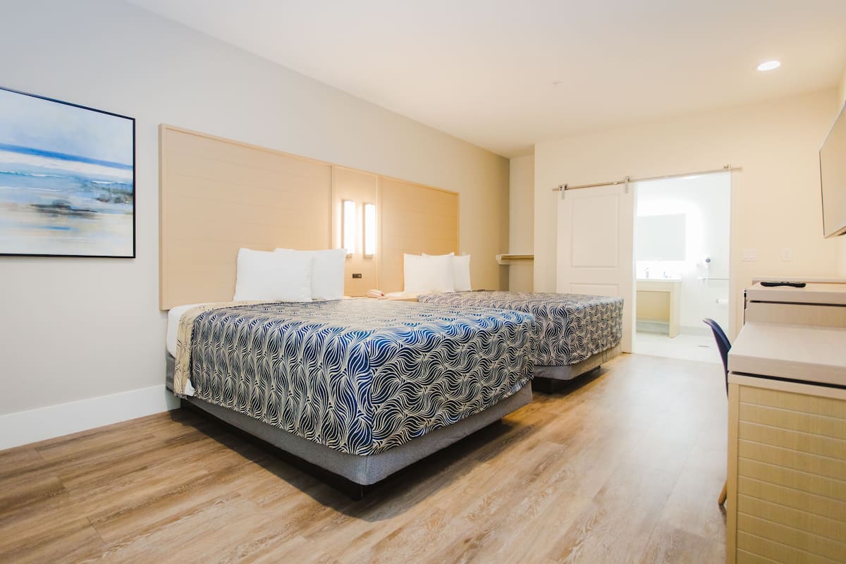 A modern hotel room with two beds, a wooden floor, a large window, and a desk.