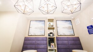 A hotel room with a modern geometric chandelier, two large framed artwork on the walls, a purple cushioned seating area, and a small shelf with various items. - Palace Inn Blue Federal Road (Houston)