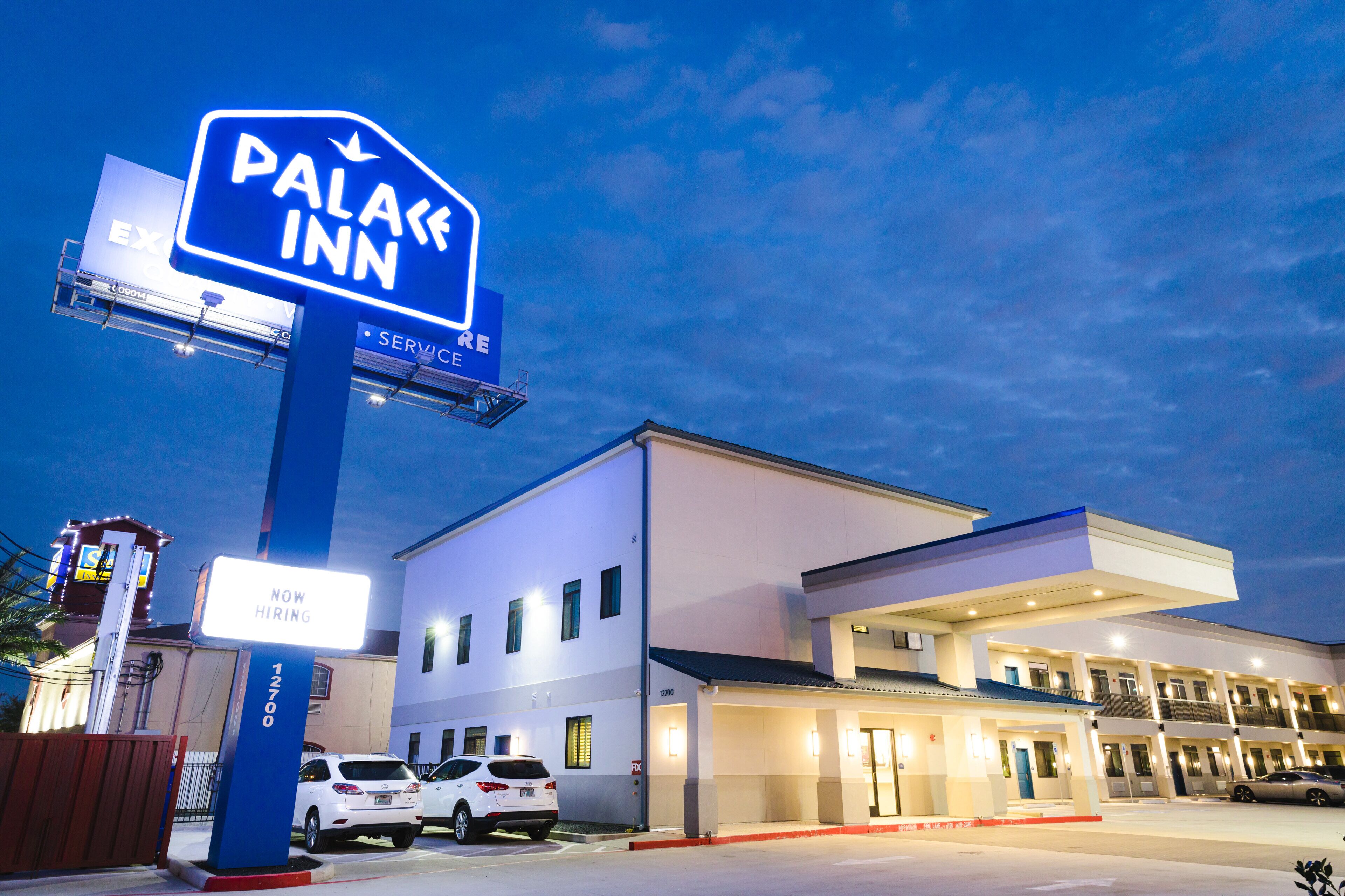 A hotel named "Palace Inn" with a "Now Hiring" sign, a parking lot with several cars, and a modern building facade.