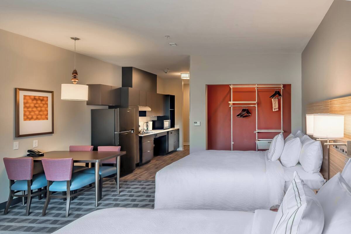 A hotel room with a bed, a desk, a chair, a wardrobe, and a kitchenette.