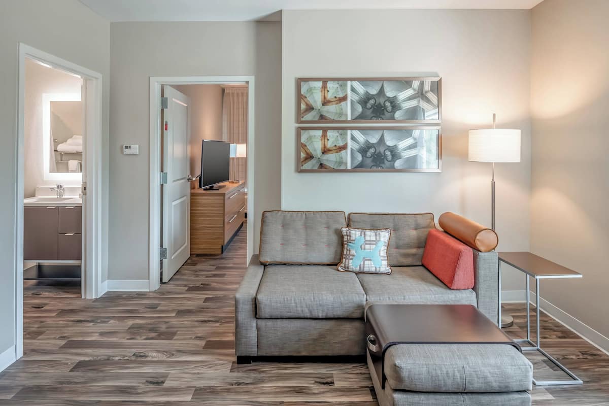 A modern living room with a grey sectional sofa, a small table, and a TV in the background.