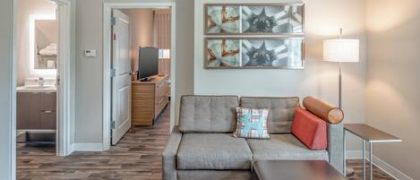 A modern living room with a grey sectional sofa, a small table, and a TV in the background.