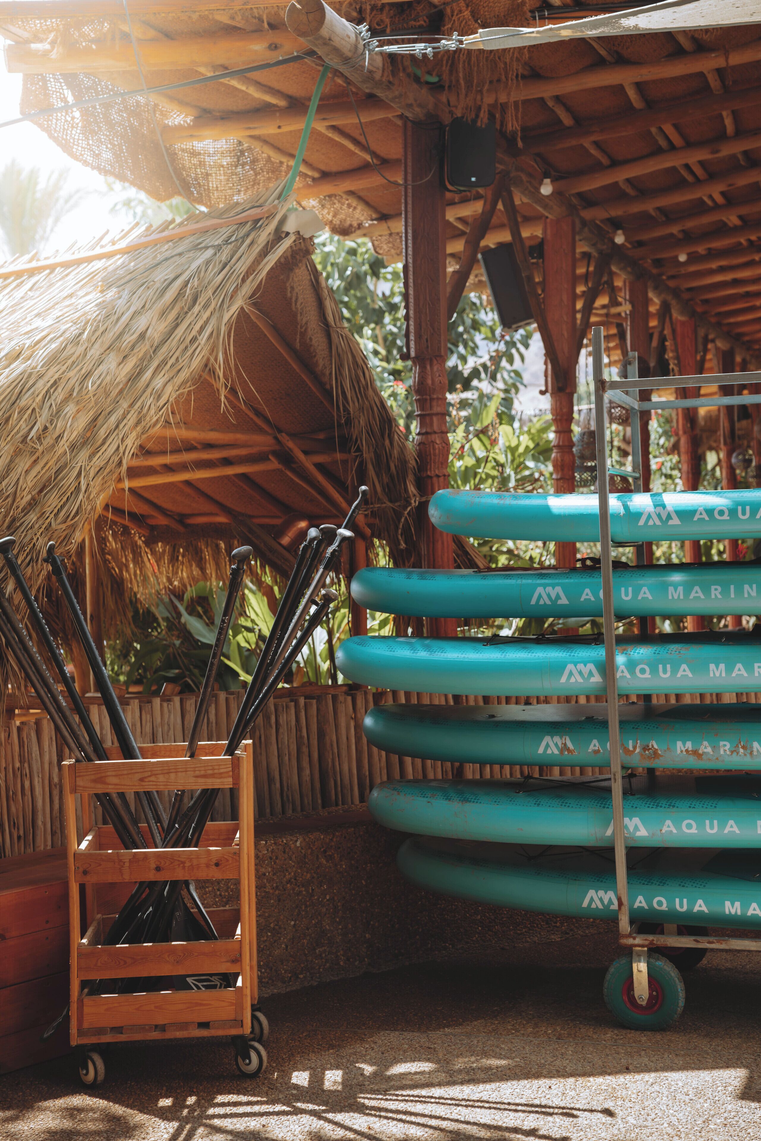 A wooden cart with metal rods, a thatched roof structure, and a metal rack with blue cylindrical objects.