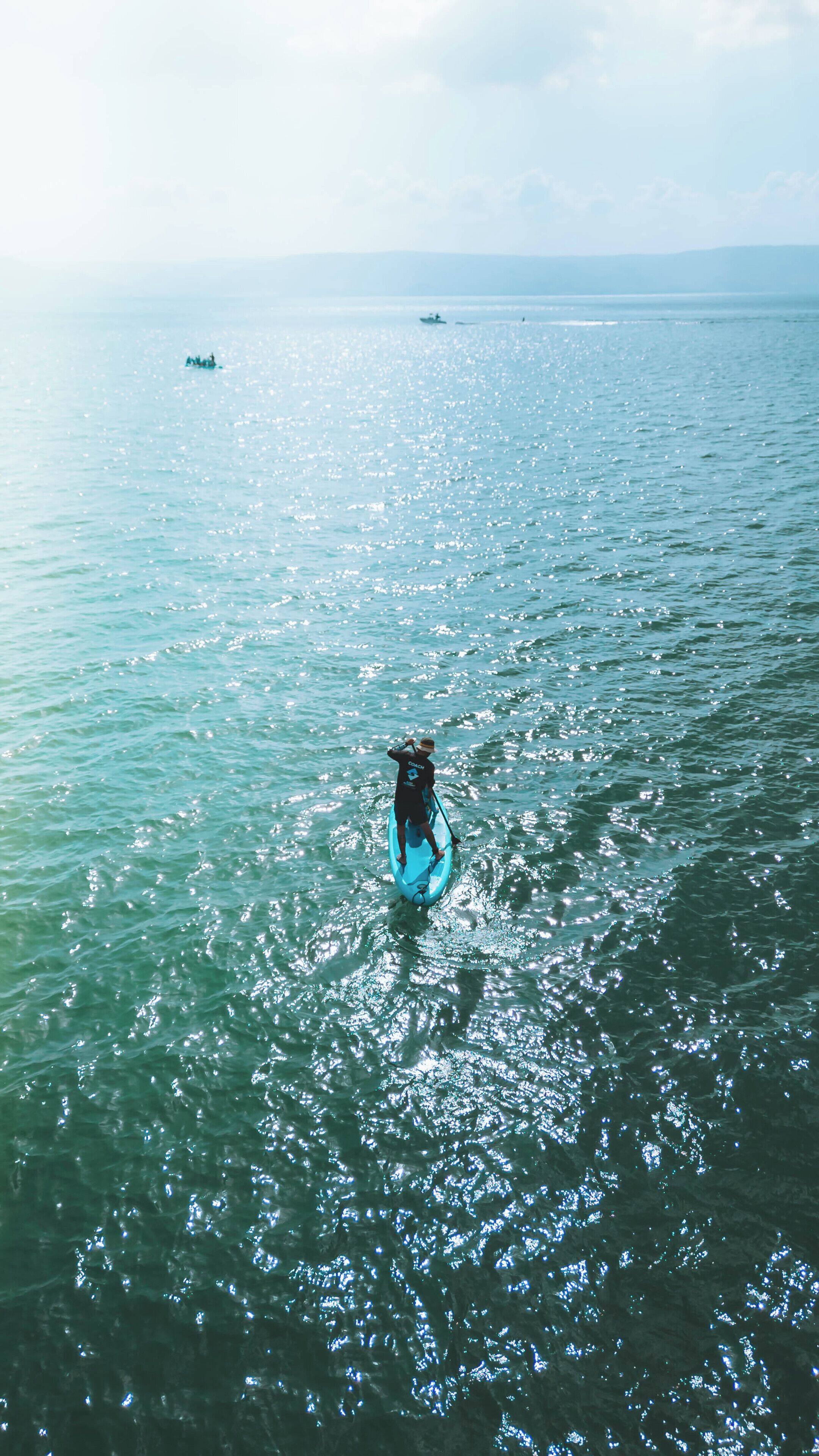 Une personne dans un kayak bleu sur une étendue d’eau calme, avec un bateau au loin et un ciel dégagé.
