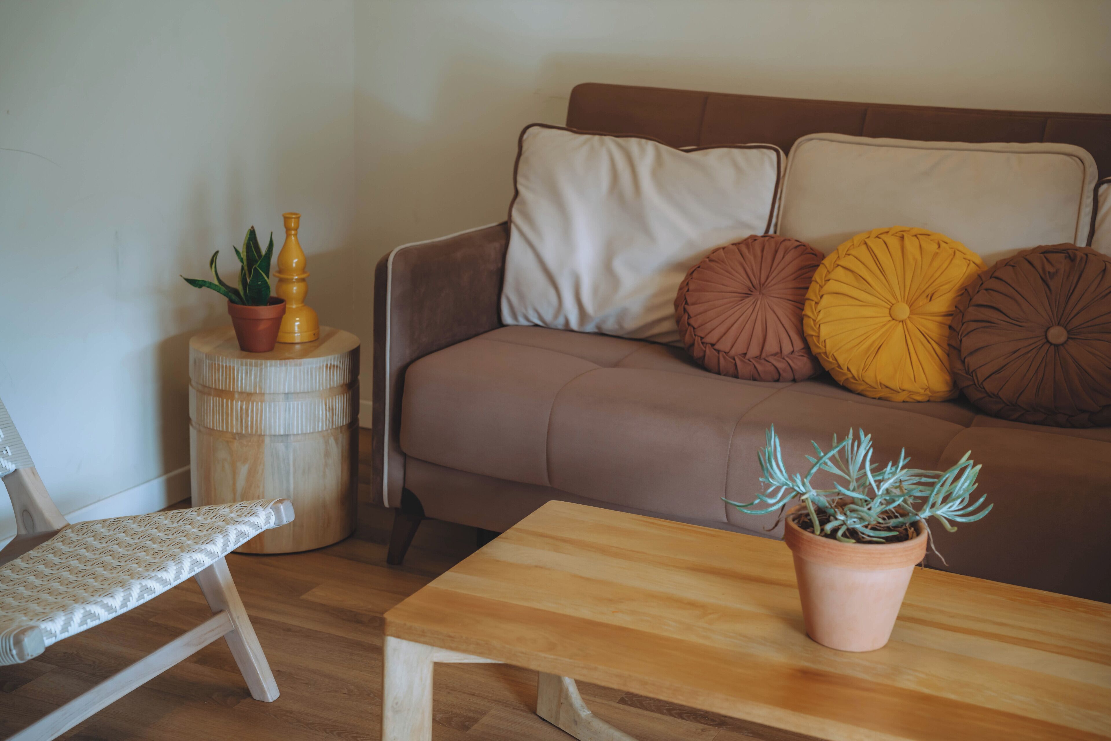 A living room with a brown sofa, a wooden coffee table, a chair, and a potted plant.