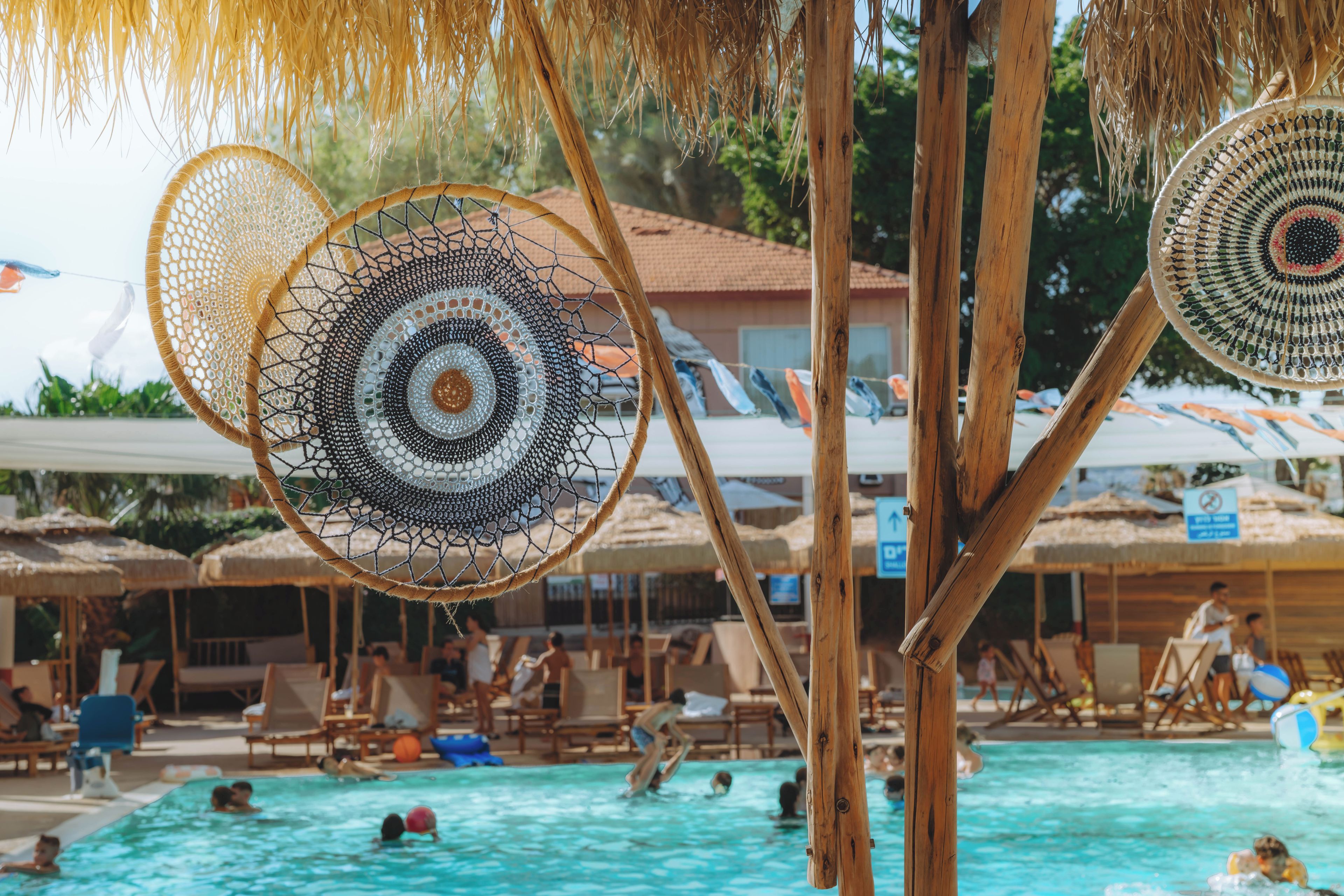 A pool area with multiple lounge chairs and umbrellas, surrounded by wooden structures and a building in the background.