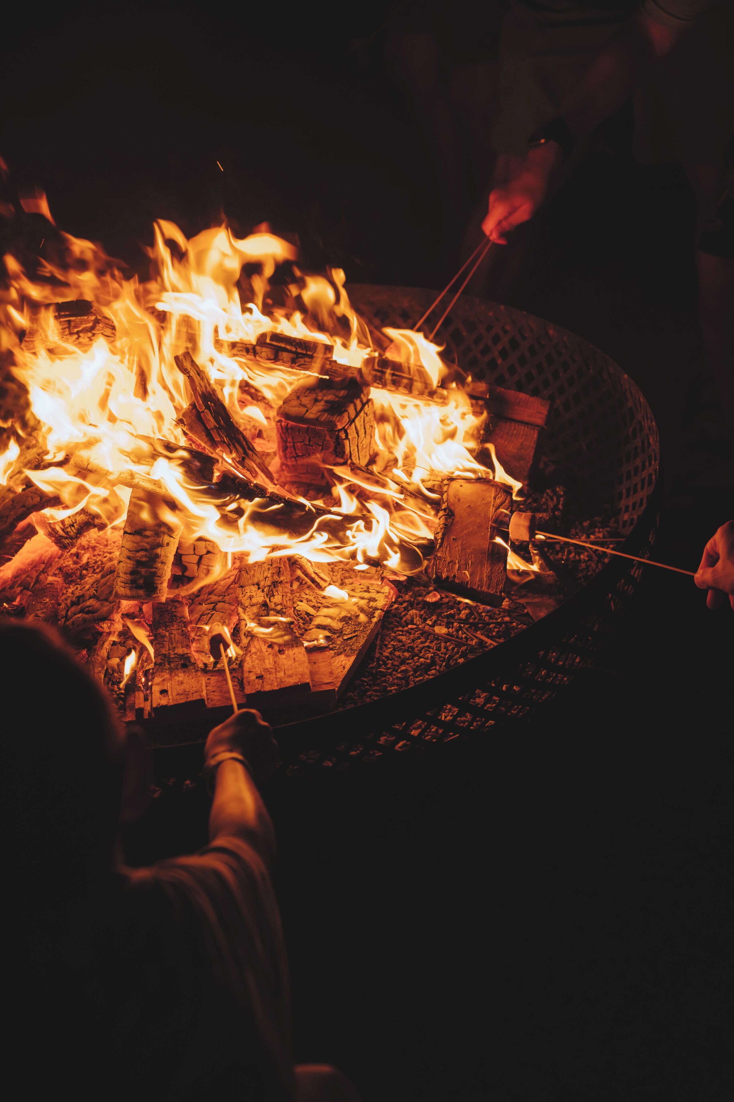A campfire with logs and flames, surrounded by people.