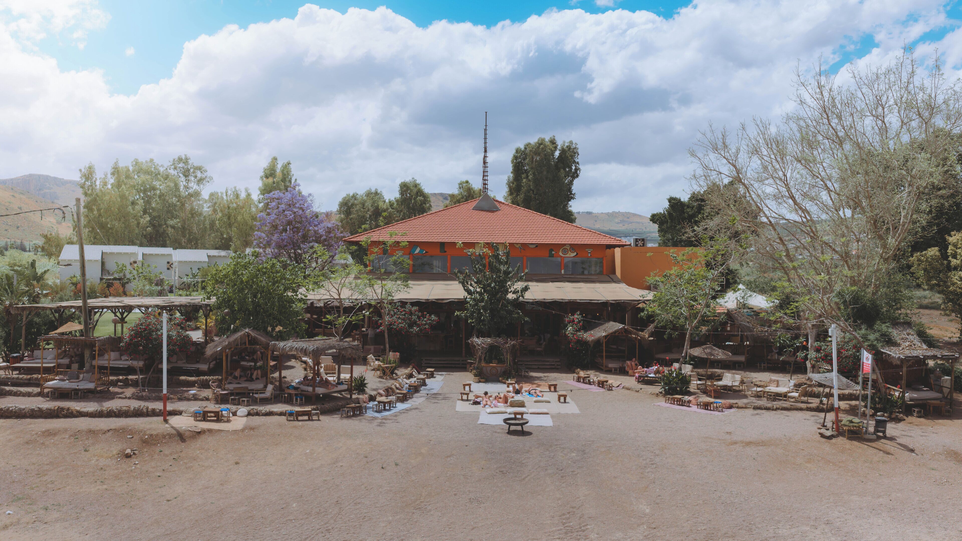 A building with a red roof, surrounded by outdoor seating areas and trees.