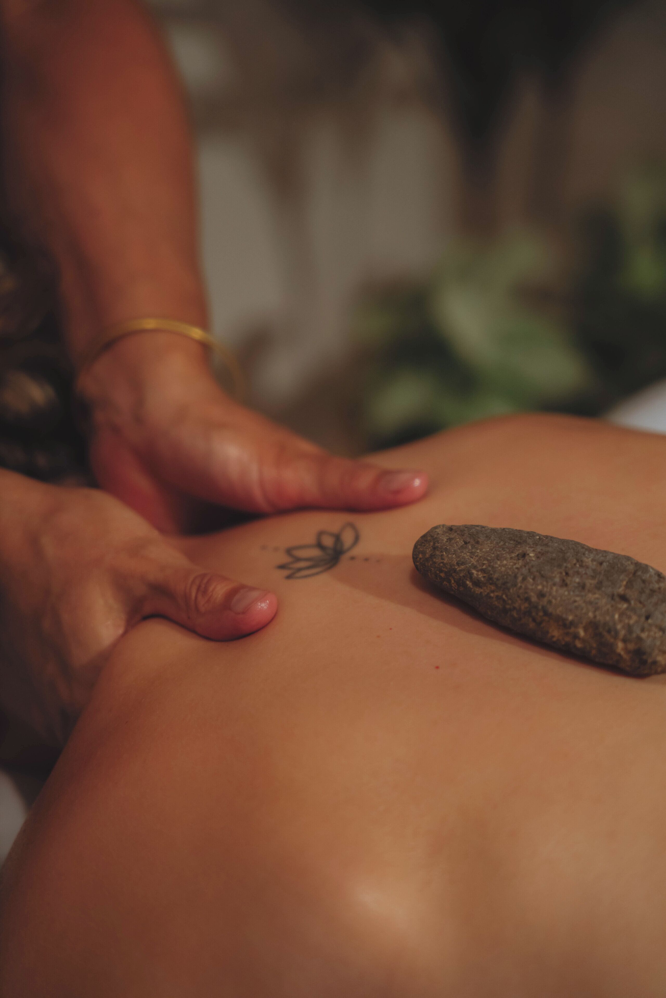 A close-up of hands on a person's back with a rock and a tattoo.