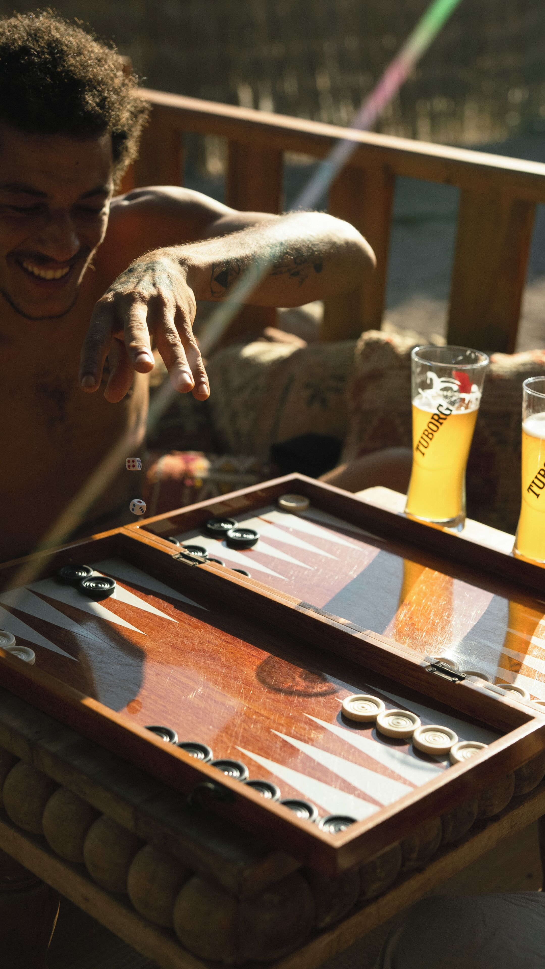 Une vue rapprochée d’un jeu de backgammon avec des dés et des pions, une table en bois et deux verres de bière.