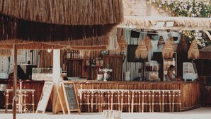 A poolside bar area with a thatched roof, wooden furniture, and a view of the pool. - Solaya Kineret (Migdal)