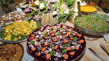 Un buffet proposant une variété de plats, notamment un grand plat de salade de fruits, une salade composée de légumes verts et de noix, ainsi que d’autres aliments variés.