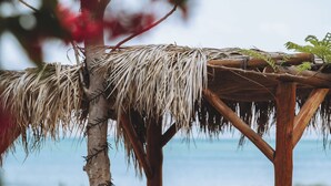 A wooden structure with a thatched roof, a person lying on a lounge chair, and a beach view. - Solaya Kineret (Migdal)