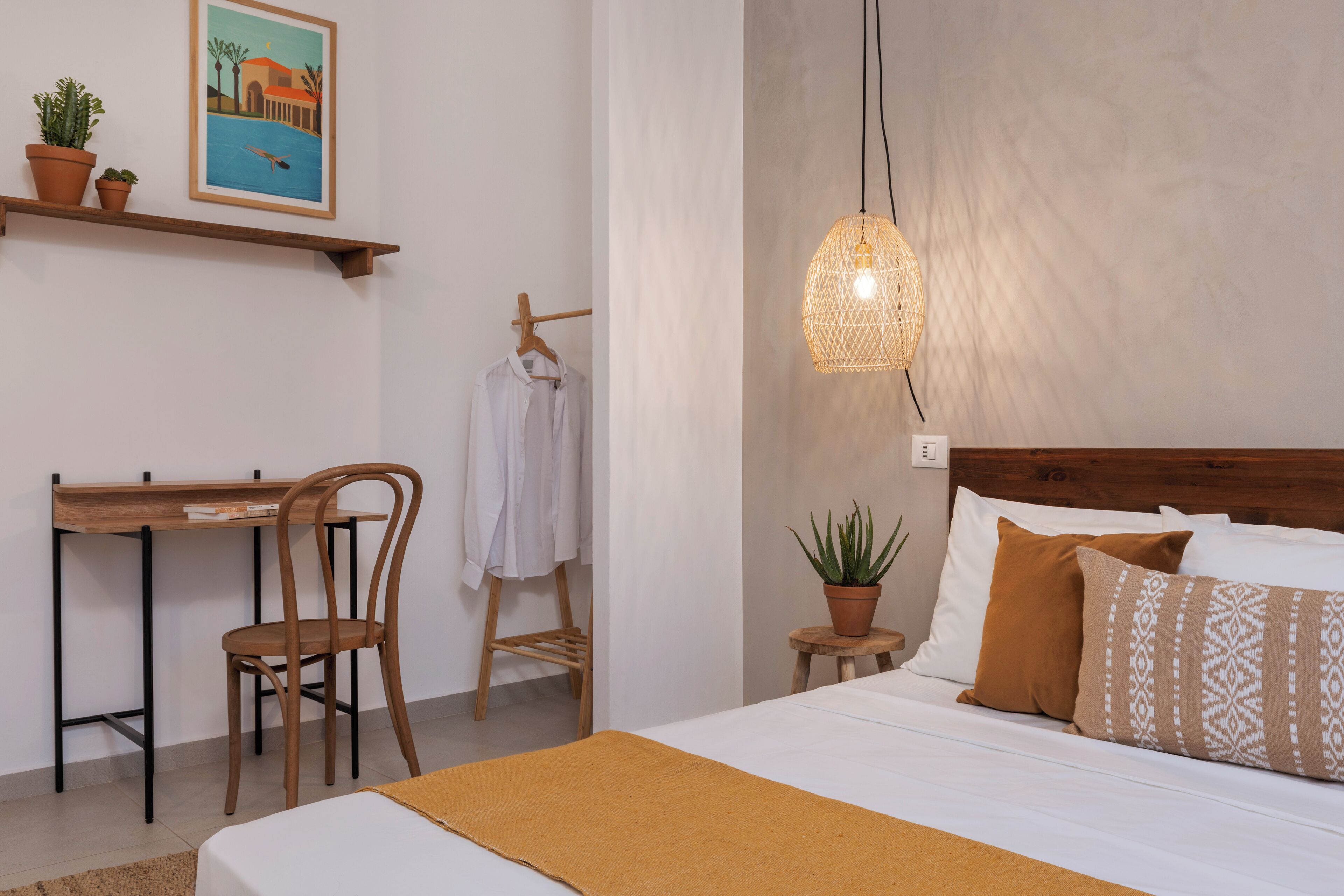 Un dormitorio con cama, escritorio, silla, lámpara colgante y estante de pared con plantas.